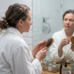 Femme examinant sa brosse à cheveux remplie de cheveux perdus dans une salle de bain, illustrant la chute de cheveux quotidienne