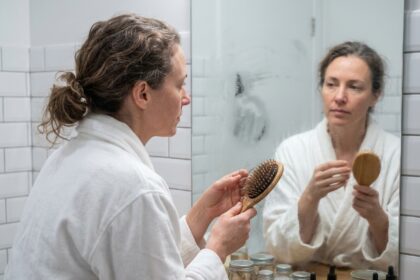 Femme examinant sa brosse à cheveux remplie de cheveux perdus dans une salle de bain, illustrant la chute de cheveux quotidienne