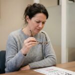 Femme tenant ses lunettes et examinant un tableau de vision chez l'opticien avant de changer de monture