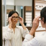 Femme essayant des lunettes tortoiseshell dans une boutique optique moderne avec rangées de montures en arrière-plan