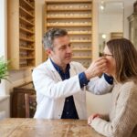 Opticien indépendant ajustant des lunettes sur une cliente dans une boutique artisanale aux étagères en bois garnies de montures
